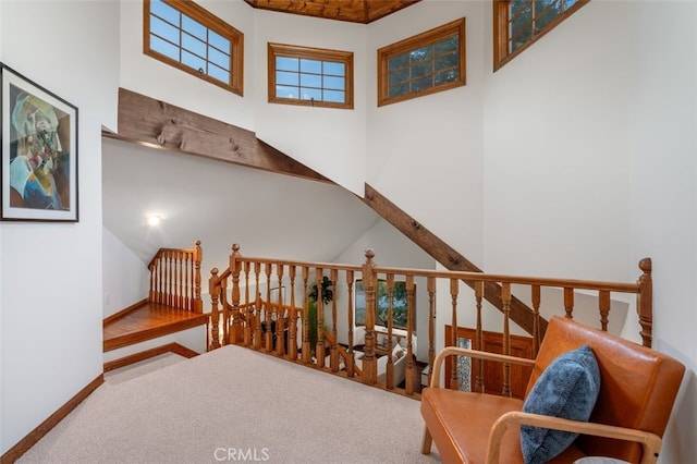 living area with a high ceiling, an upstairs landing, carpet floors, and baseboards