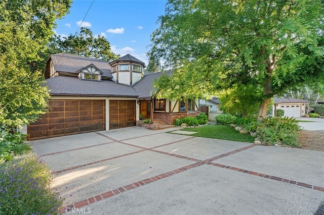 tudor-style house featuring driveway, an attached garage, and roof with shingles