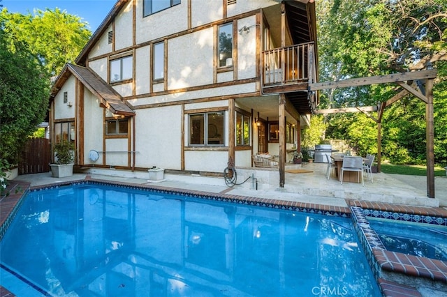 rear view of property with a patio area, stucco siding, a pool with connected hot tub, and a balcony