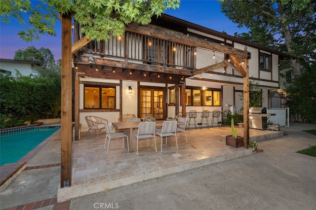rear view of house featuring a balcony, a patio, an outdoor pool, and stucco siding