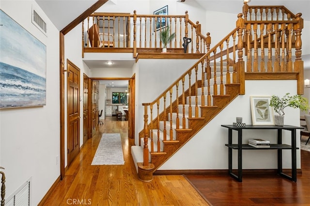 stairs with wood finished floors, a towering ceiling, and baseboards