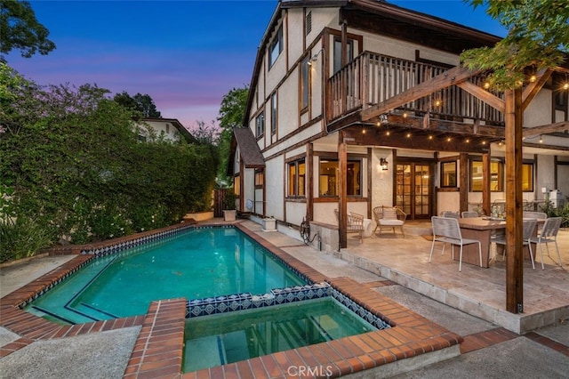 pool at dusk with a patio area and a pool with connected hot tub