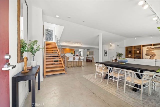 dining room with stairway, track lighting, concrete flooring, and lofted ceiling