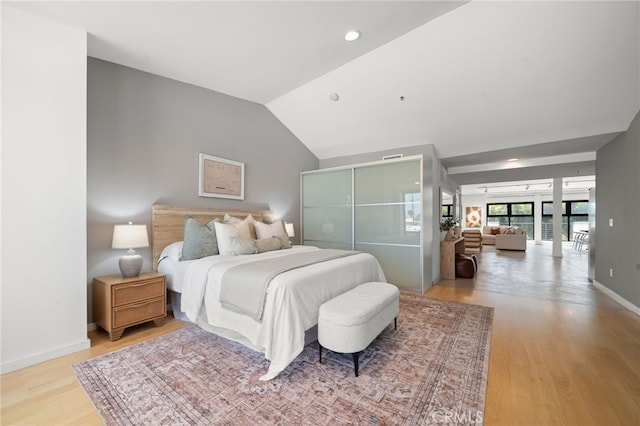 bedroom with light wood-style floors, lofted ceiling, and baseboards