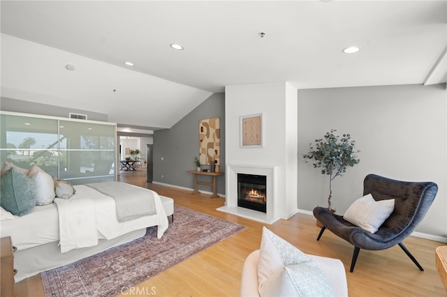 bedroom featuring wood finished floors, lofted ceiling, recessed lighting, a glass covered fireplace, and baseboards
