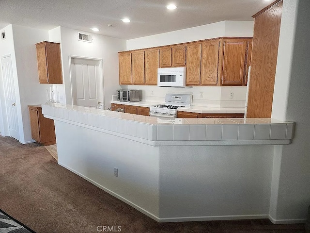kitchen with white appliances, brown cabinetry, carpet, recessed lighting, and tile countertops