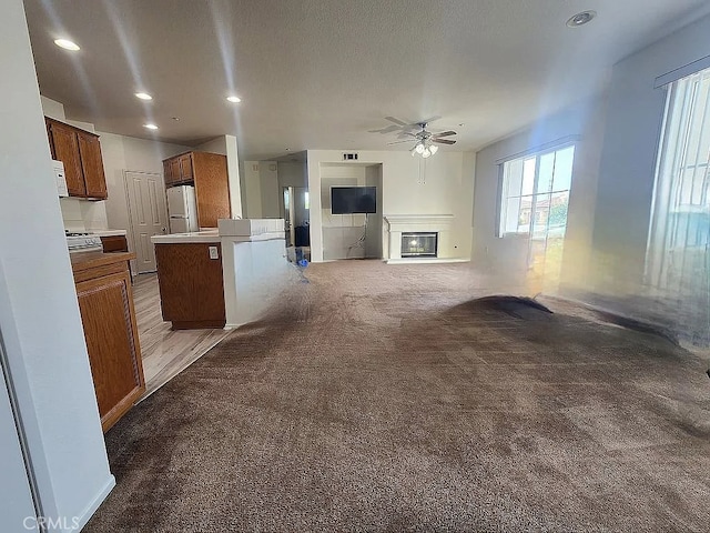 kitchen featuring white appliances, a ceiling fan, carpet flooring, open floor plan, and a glass covered fireplace