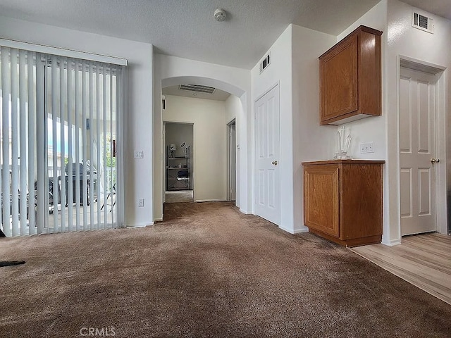 corridor with arched walkways, light carpet, and baseboards
