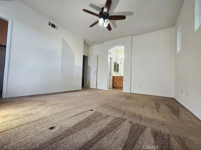empty room featuring ceiling fan, arched walkways, light colored carpet, and baseboards