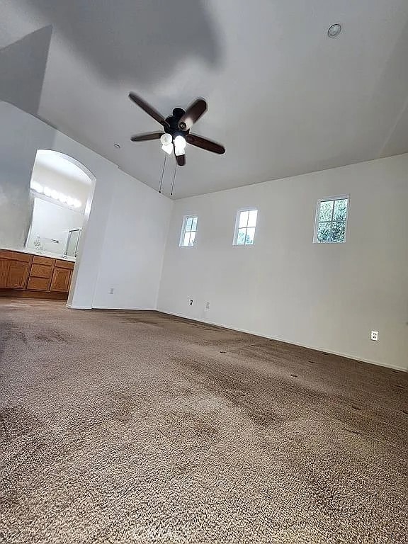 unfurnished room featuring a ceiling fan, carpet flooring, and arched walkways
