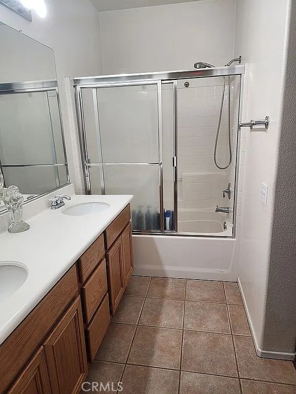 full bathroom featuring combined bath / shower with glass door, tile patterned floors, double vanity, and baseboards