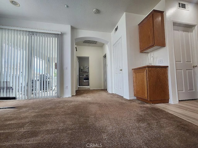 corridor with arched walkways, light colored carpet, and baseboards