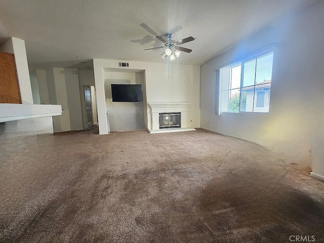 unfurnished living room featuring a glass covered fireplace, a ceiling fan, carpet floors, a textured ceiling, and baseboards