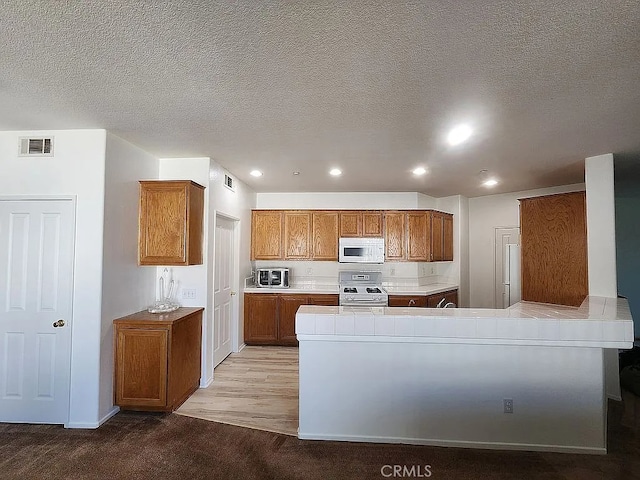 kitchen with white appliances, brown cabinets, a textured ceiling, recessed lighting, and a peninsula