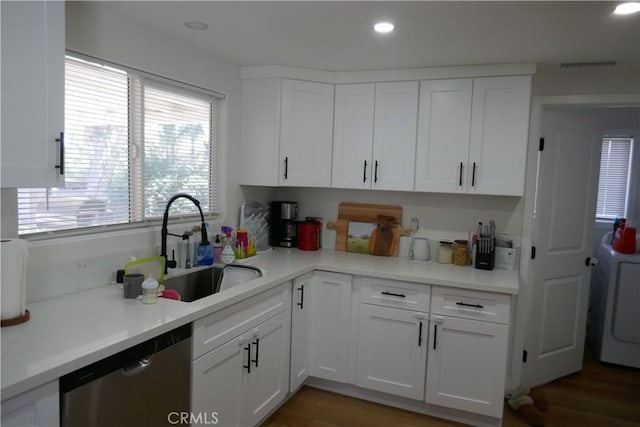 kitchen with stainless steel dishwasher, washer / clothes dryer, a sink, white cabinets, and light countertops