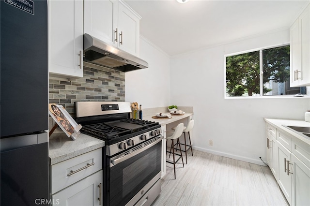 617 Cedar Ave Unit 11, Long Beach, CA 90802 - kitchen with stainless steel gas stove, under cabinet range hood, freestanding refrigerator, backsplash, and white cabinetry
