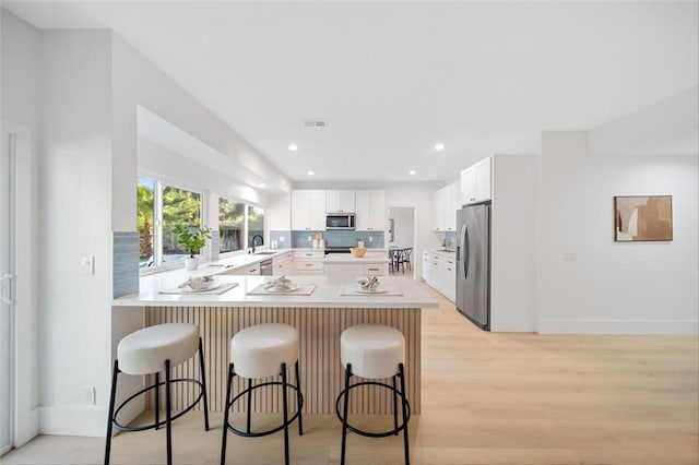 30901 Wellington Cir, Temecula, CA 92591 - kitchen with stainless steel appliances, a peninsula, a kitchen bar, light wood-style floors, and white cabinetry