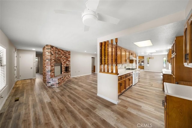 410 N Las Flores Dr, Nipomo, CA 93444 - kitchen with gas range gas stove, open floor plan, brown cabinetry, a brick fireplace, and light wood-type flooring