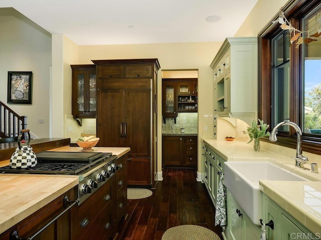 kitchen featuring a sink, dark wood-type flooring, stainless steel gas cooktop, tasteful backsplash, and glass insert cabinets