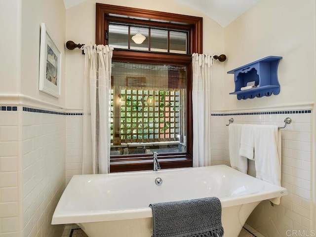 full bathroom with tile walls, a freestanding tub, and a wainscoted wall