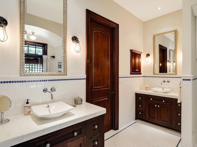 full bathroom with tile walls, wainscoting, and two vanities