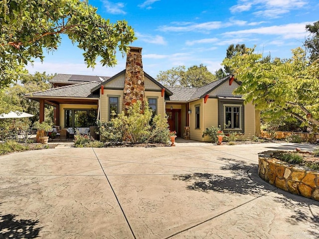 rear view of house with a chimney, curved driveway, and an outdoor hangout area