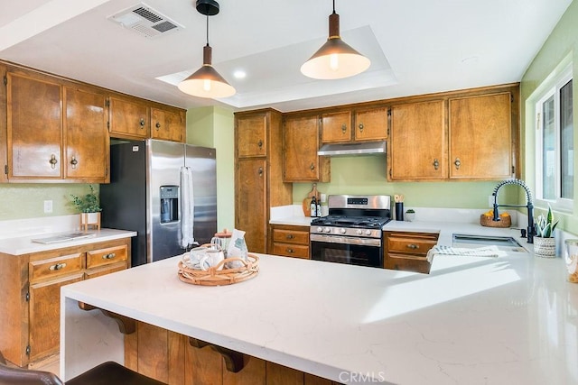 kitchen with appliances with stainless steel finishes, under cabinet range hood, a sink, light countertops, and brown cabinets