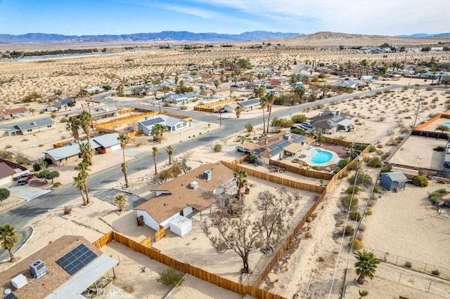 aerial view of sparsely populated area featuring a desert landscape, a mountain backdrop, a pool, and nearby suburban area