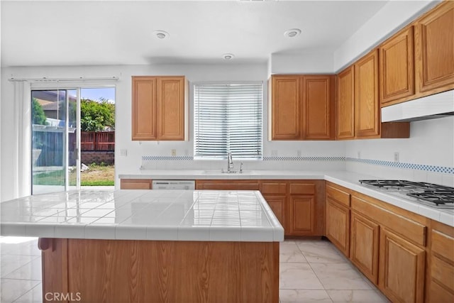 kitchen with light marble finish flooring, gas cooktop, under cabinet range hood, tile counters, and dishwasher