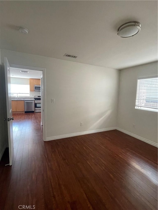 spare room with dark wood-type flooring, a sink, baseboards, and a smoke detector