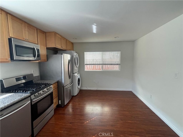 kitchen featuring appliances with stainless steel finishes, stacked washing machine and dryer, dark wood-style flooring, and baseboards