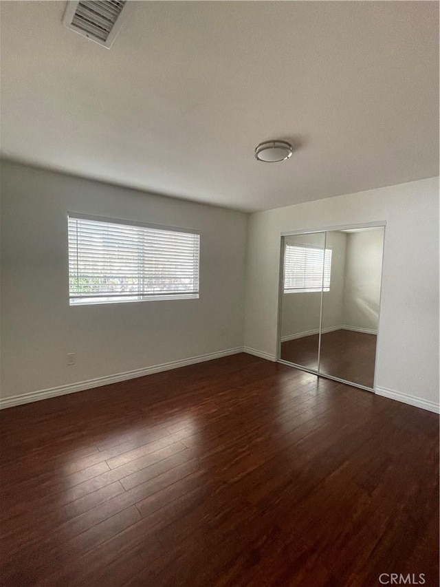 unfurnished bedroom with dark wood-style flooring, baseboards, and a closet