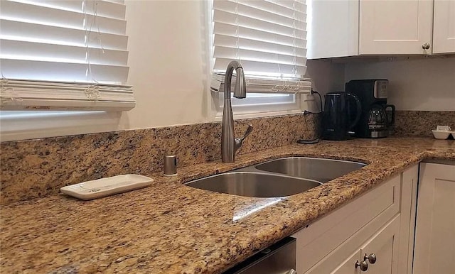 kitchen view of a sink, white cabinetry, and light stone counters