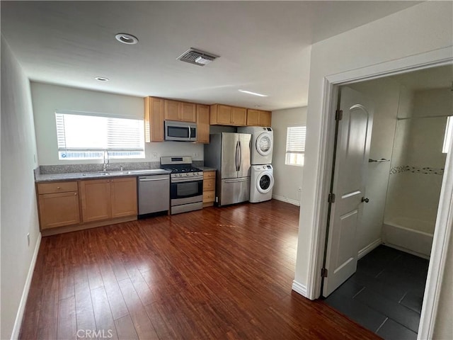 kitchen featuring appliances with stainless steel finishes, stacked washer and clothes dryer, dark wood-style flooring, baseboards, and a sink