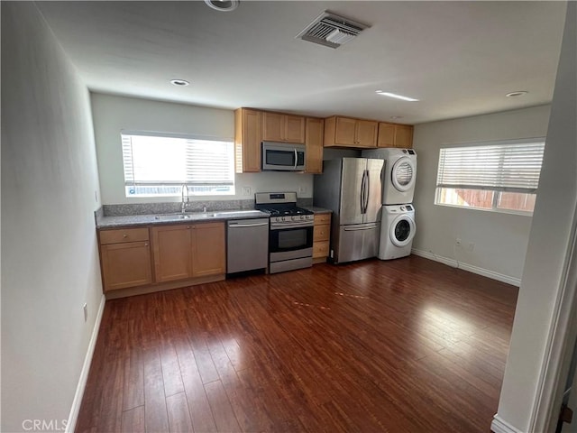 kitchen with stainless steel appliances, stacked washer / dryer, dark wood-style floors, baseboards, and healthy amount of natural light