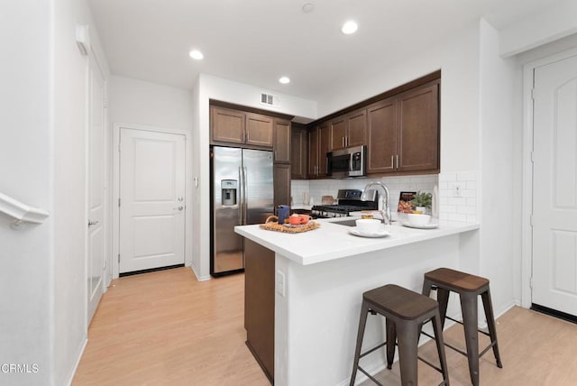 kitchen featuring stainless steel appliances, light wood finished floors, a kitchen breakfast bar, a peninsula, and tasteful backsplash