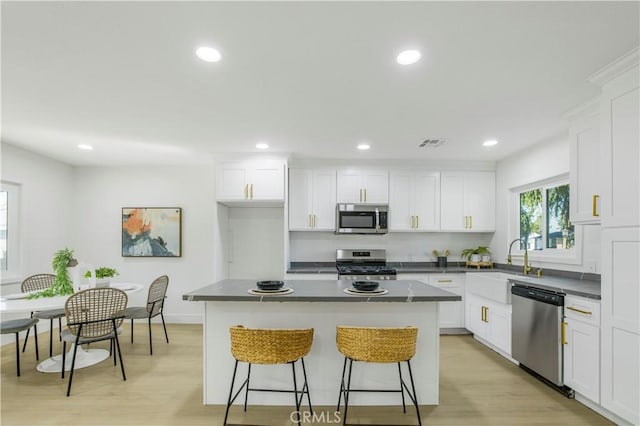 kitchen featuring stainless steel appliances, dark countertops, a kitchen breakfast bar, a kitchen island, and recessed lighting