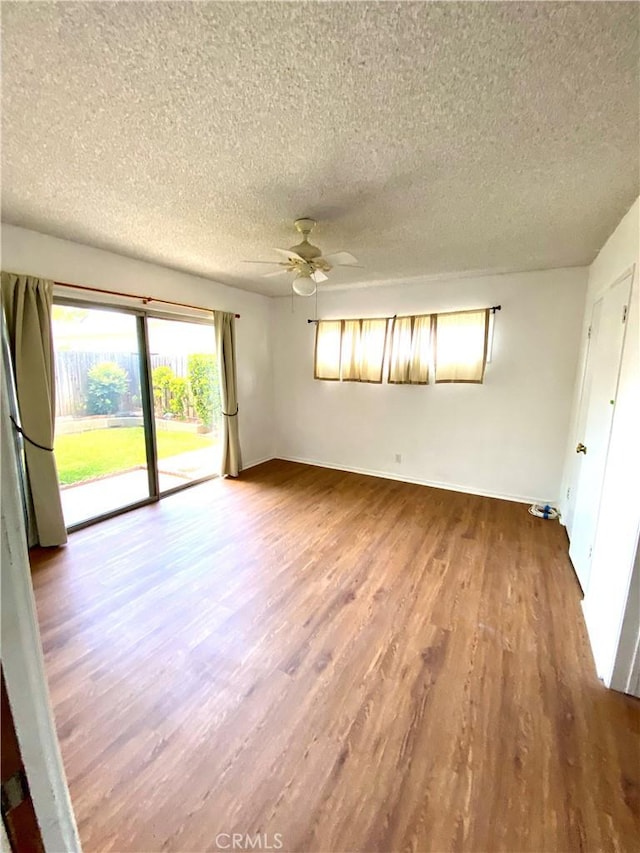 spare room with a textured ceiling, ceiling fan, wood finished floors, and baseboards