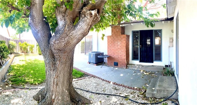 property entrance featuring central air condition unit, fence, brick siding, stucco siding, and a patio