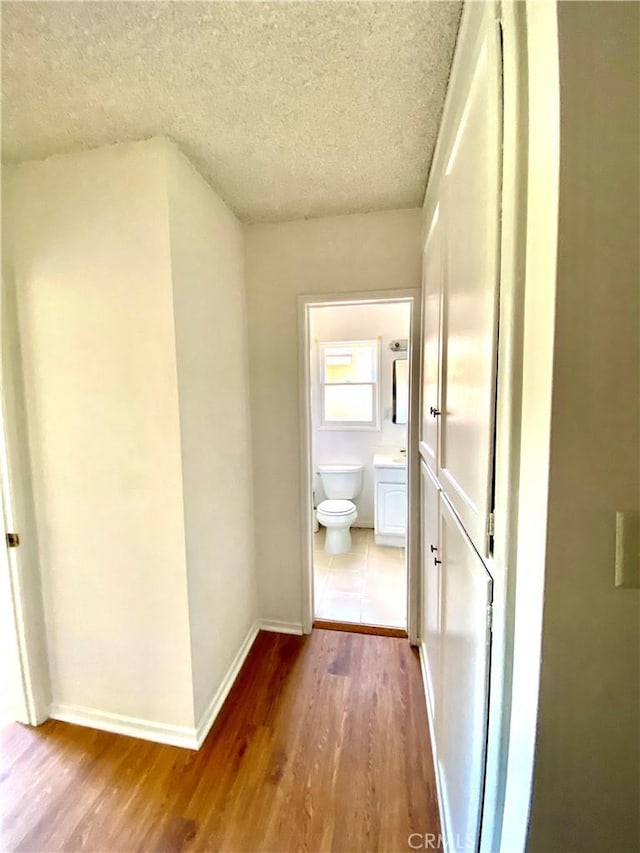 corridor featuring wood finished floors, a textured ceiling, and baseboards
