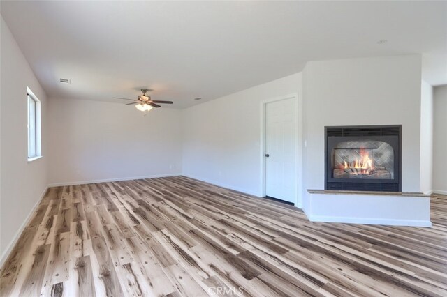 43038 Glacier Ln, Coarsegold, CA 93614 - unfurnished living room featuring light wood finished floors, a glass covered fireplace, baseboards, and a ceiling fan
