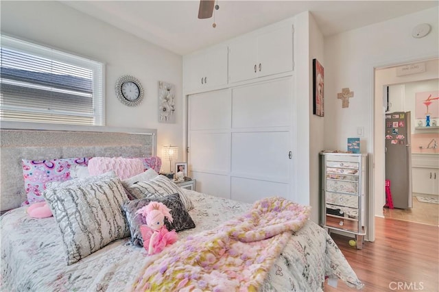 bedroom with freestanding refrigerator, wood finished floors, a closet, and ceiling fan