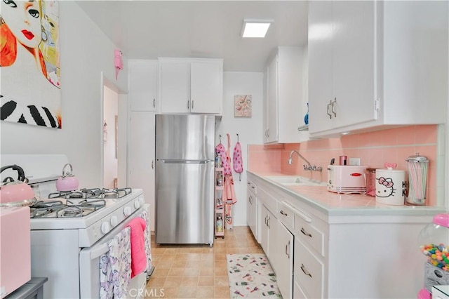 kitchen featuring freestanding refrigerator, gas range gas stove, a sink, light countertops, and white cabinets