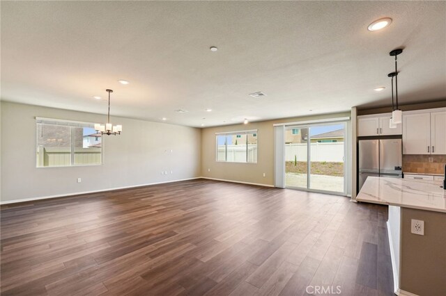 unfurnished living room featuring dark wood-type flooring, a chandelier, recessed lighting, and baseboards