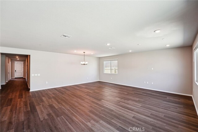 empty room featuring a chandelier, recessed lighting, dark wood-type flooring, and baseboards