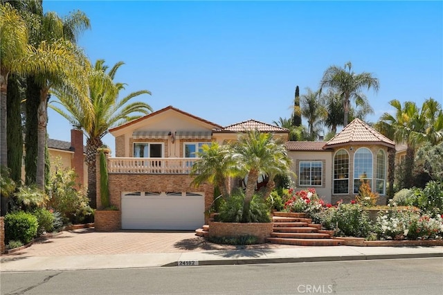 24182 Torena Cir, Mission Viejo, CA 92691 - mediterranean / spanish-style home with decorative driveway, an attached garage, stucco siding, a balcony, and a tiled roof