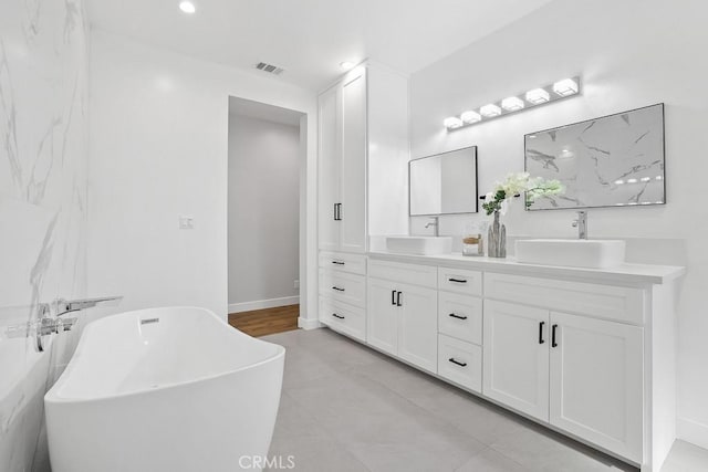 bathroom featuring double vanity, a freestanding tub, recessed lighting, and baseboards