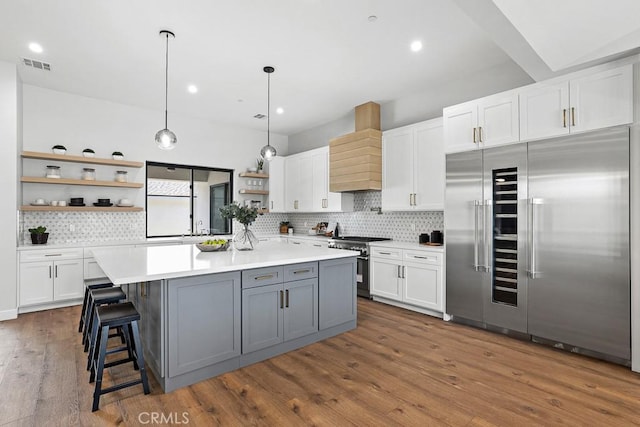 kitchen with high quality appliances, open shelves, custom range hood, backsplash, and white cabinets