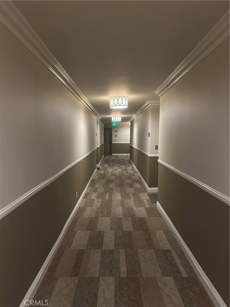 hall with carpet flooring, ornamental molding, and baseboards