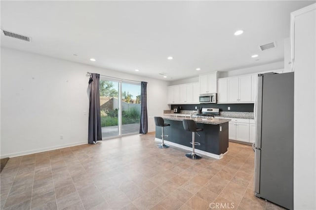36927 Arezzo Ct, Beaumont, CA 92223 - kitchen featuring appliances with stainless steel finishes, white cabinets, a kitchen bar, recessed lighting, and light stone countertops